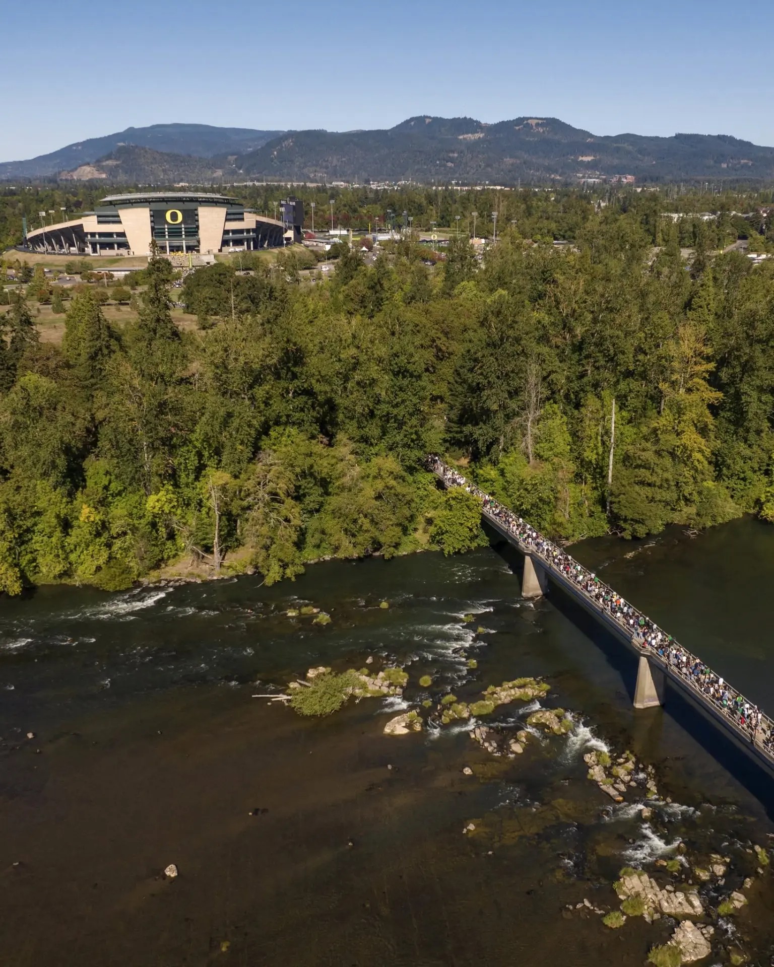 Walkers crossing the Willamette on the pedestrian bridge, with the stadium and the hills beyond
